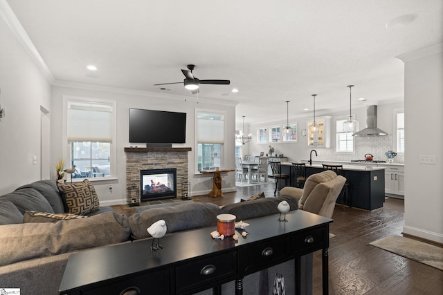 living room featuring dark wood-type flooring, sink, ceiling fan, crown molding, and a fireplace