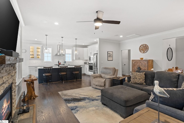 living room with a stone fireplace, ceiling fan, dark hardwood / wood-style floors, and crown molding