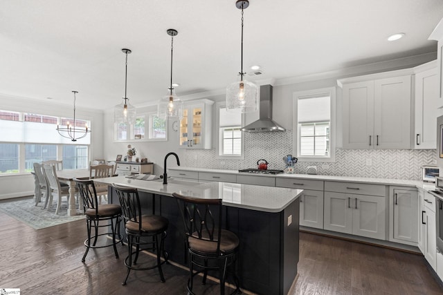 kitchen with hanging light fixtures, an island with sink, dark hardwood / wood-style floors, wall chimney range hood, and a breakfast bar