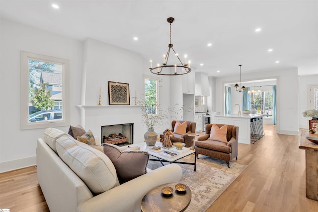 living room with light hardwood / wood-style floors, a healthy amount of sunlight, sink, and an inviting chandelier