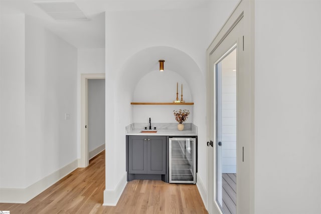 bar with beverage cooler, sink, light wood-type flooring, and gray cabinetry