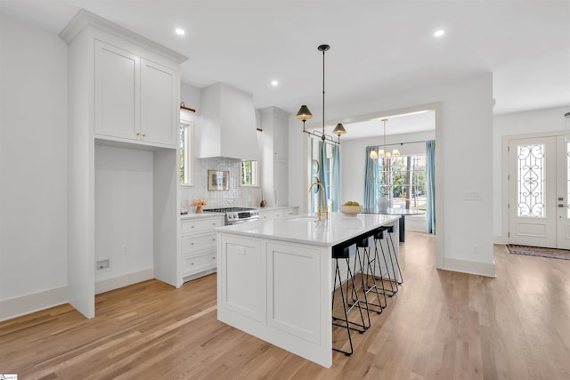 kitchen with light hardwood / wood-style floors, hanging light fixtures, sink, a kitchen island with sink, and white cabinetry