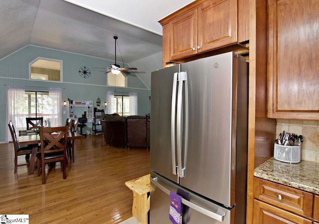 kitchen featuring light stone counters, stainless steel refrigerator, vaulted ceiling, hardwood / wood-style flooring, and ceiling fan