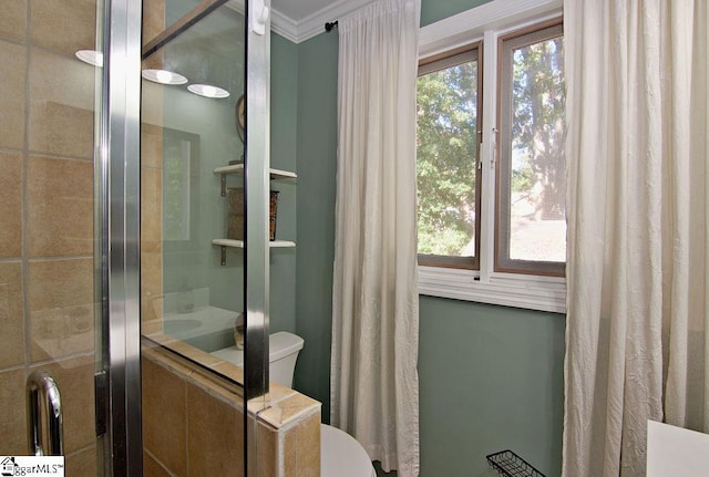 bathroom with plenty of natural light, toilet, a tile shower, and ornamental molding