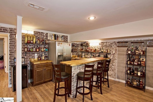 bar featuring stainless steel fridge, wood counters, brick wall, and light wood-type flooring