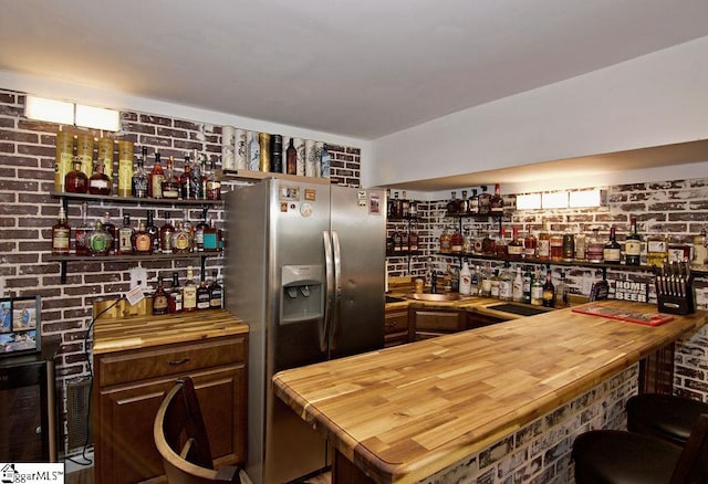 kitchen featuring stainless steel refrigerator with ice dispenser, sink, wood counters, dark brown cabinets, and brick wall