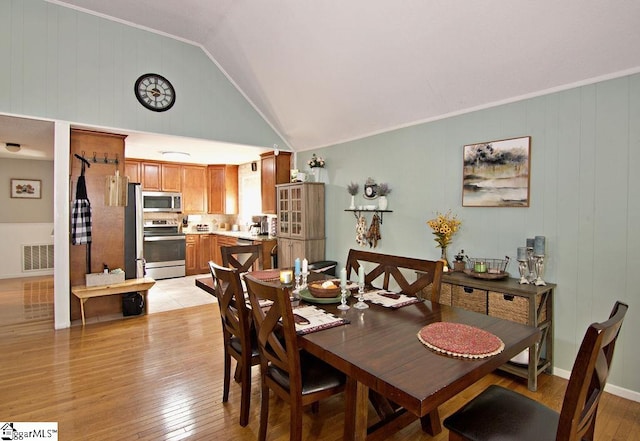 dining area featuring lofted ceiling, ornamental molding, and light hardwood / wood-style flooring