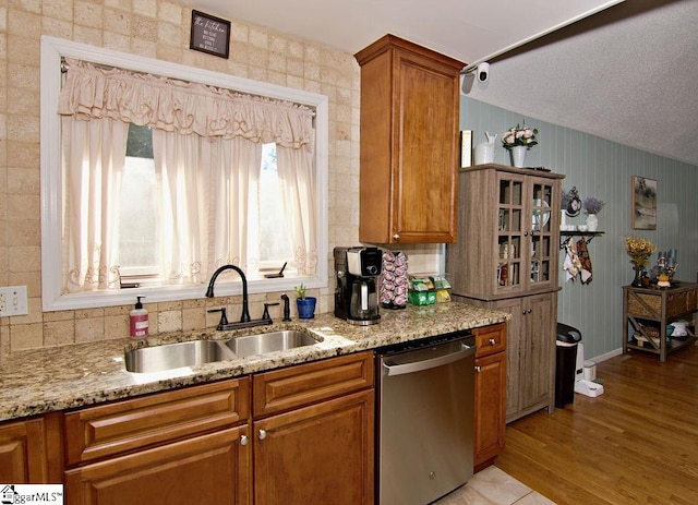 kitchen featuring light stone counters, sink, light wood-type flooring, and dishwasher