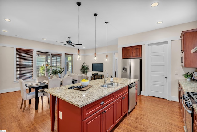 kitchen featuring sink, stainless steel appliances, ceiling fan, light stone countertops, and a center island with sink