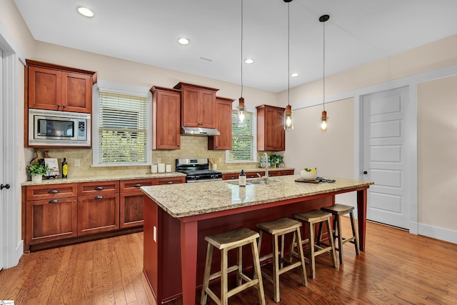 kitchen featuring sink, stainless steel appliances, a center island with sink, and hanging light fixtures