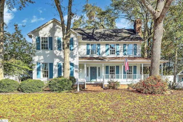 colonial home featuring covered porch and a front lawn