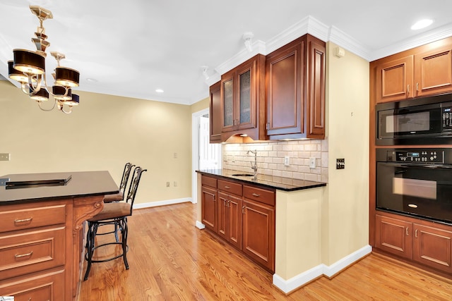 kitchen with a kitchen bar, black appliances, a chandelier, crown molding, and light wood-type flooring