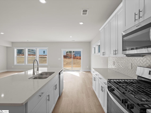 kitchen with appliances with stainless steel finishes, sink, white cabinets, and light hardwood / wood-style flooring