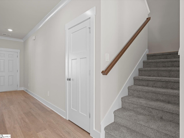 stairway with crown molding and wood-type flooring