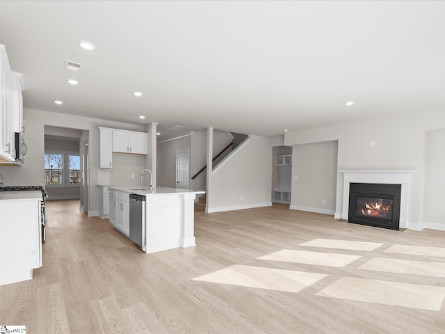 kitchen featuring sink, a kitchen island with sink, white cabinetry, stainless steel appliances, and light wood-type flooring