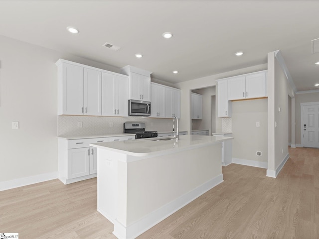 kitchen featuring light wood-type flooring, stainless steel appliances, an island with sink, and white cabinets