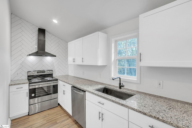 kitchen with appliances with stainless steel finishes, wall chimney exhaust hood, sink, light hardwood / wood-style flooring, and white cabinets