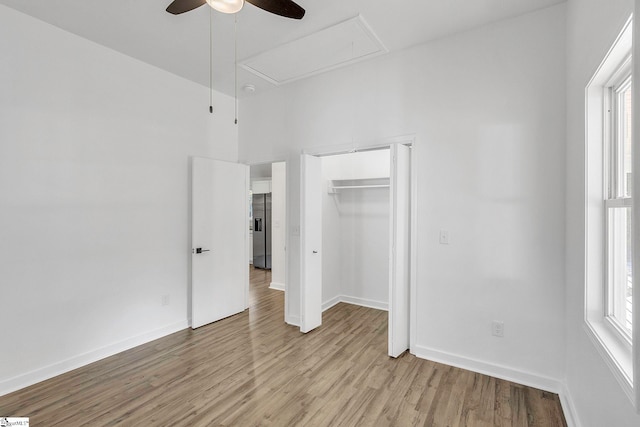 unfurnished bedroom featuring multiple windows, ceiling fan, light hardwood / wood-style flooring, and stainless steel refrigerator with ice dispenser