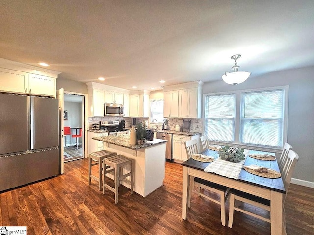 kitchen featuring white cabinets, a kitchen island, appliances with stainless steel finishes, and hanging light fixtures