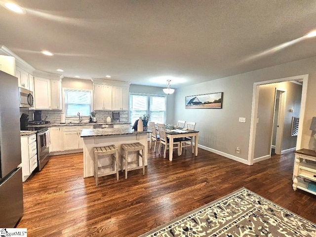 kitchen with decorative backsplash, dark hardwood / wood-style floors, a kitchen island, white cabinetry, and appliances with stainless steel finishes