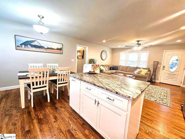 kitchen featuring dark wood-type flooring, a center island, ceiling fan, light stone countertops, and white cabinetry