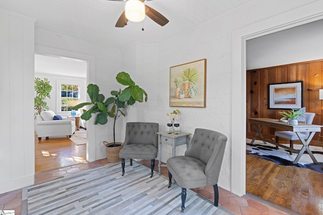 sitting room with wood walls, light wood-type flooring, and ceiling fan