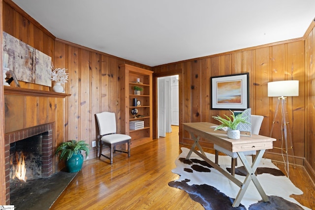 office space with light hardwood / wood-style floors, built in shelves, ornamental molding, a fireplace, and wooden walls