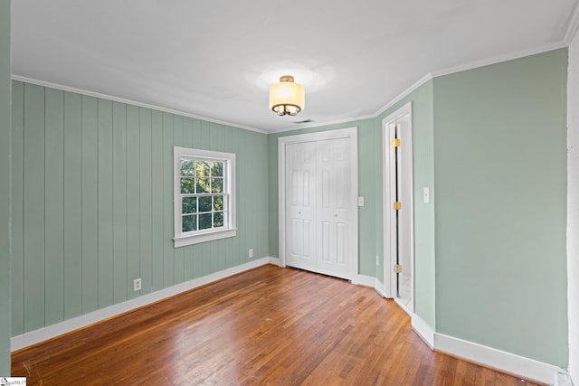 unfurnished bedroom featuring a closet, hardwood / wood-style floors, wood walls, and crown molding