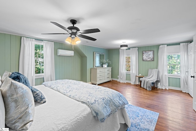 bedroom with an AC wall unit, multiple windows, wood-type flooring, and ceiling fan