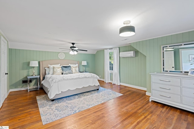 bedroom featuring ornamental molding, a wall unit AC, ceiling fan, wooden walls, and dark hardwood / wood-style flooring