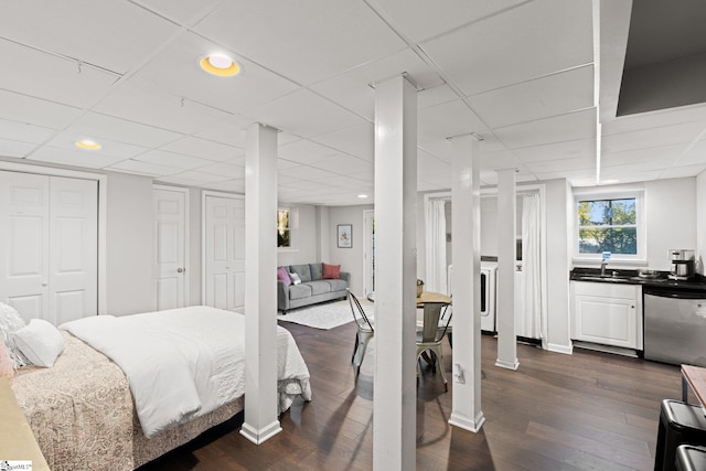 bedroom with a paneled ceiling, dark wood-type flooring, sink, and two closets