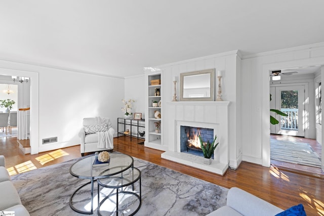 living room with built in shelves, hardwood / wood-style floors, ornamental molding, and ceiling fan