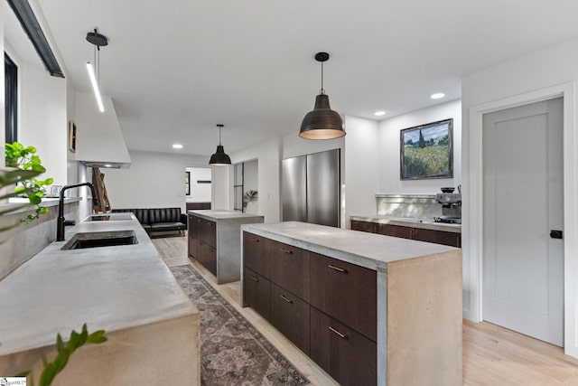 kitchen with a center island, dark brown cabinetry, hanging light fixtures, sink, and light wood-type flooring