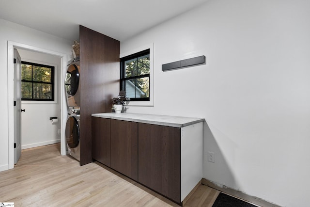 washroom featuring cabinets, stacked washer / dryer, and light wood-type flooring