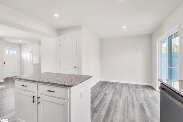 kitchen with stainless steel dishwasher, a kitchen island, light stone countertops, light hardwood / wood-style floors, and white cabinetry