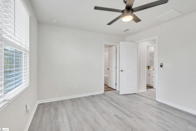 unfurnished bedroom featuring ceiling fan, light hardwood / wood-style floors, ensuite bath, and multiple windows