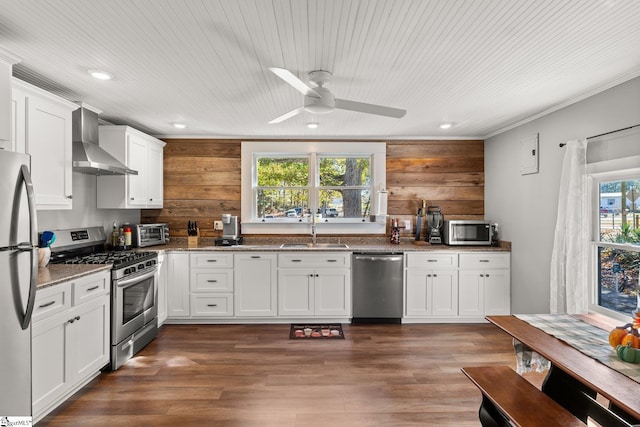 kitchen featuring appliances with stainless steel finishes, sink, white cabinets, dark stone countertops, and wall chimney exhaust hood