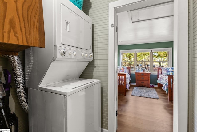 clothes washing area featuring light hardwood / wood-style flooring, wood walls, and stacked washer and clothes dryer