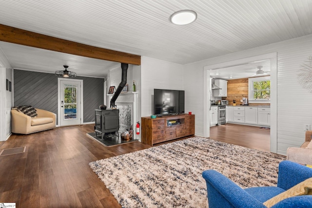 living room with a wood stove, dark hardwood / wood-style floors, wood walls, beamed ceiling, and ceiling fan