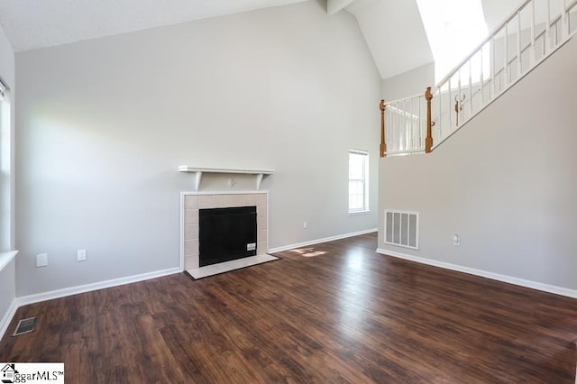 unfurnished living room with high vaulted ceiling, a tiled fireplace, and dark hardwood / wood-style flooring