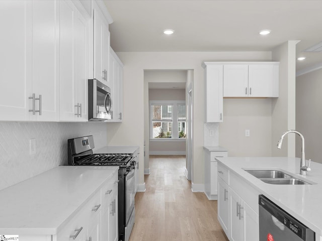 kitchen with white cabinets, sink, decorative backsplash, light wood-type flooring, and appliances with stainless steel finishes