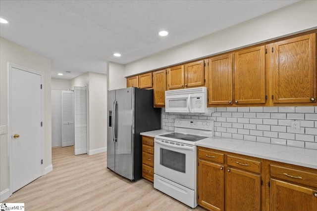 kitchen featuring white appliances, decorative backsplash, and light wood-type flooring