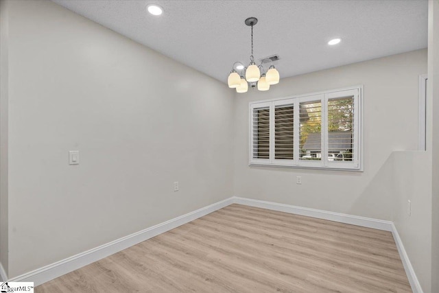 unfurnished room featuring a textured ceiling, light hardwood / wood-style flooring, and an inviting chandelier