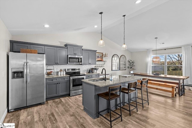 kitchen featuring sink, a center island with sink, vaulted ceiling, appliances with stainless steel finishes, and light stone countertops