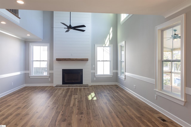 unfurnished living room with dark hardwood / wood-style flooring, a towering ceiling, a large fireplace, and a wealth of natural light