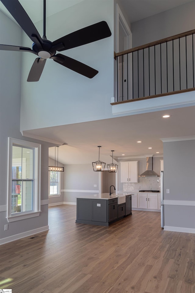 kitchen featuring wall chimney range hood, pendant lighting, fridge, wood-type flooring, and white cabinets