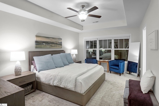 bedroom with a raised ceiling, ceiling fan, and light colored carpet