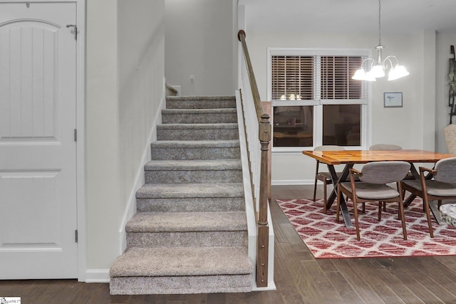 stairway with wood-type flooring and an inviting chandelier