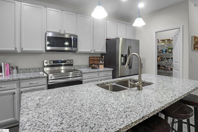 kitchen with light stone counters, stainless steel appliances, sink, pendant lighting, and an island with sink