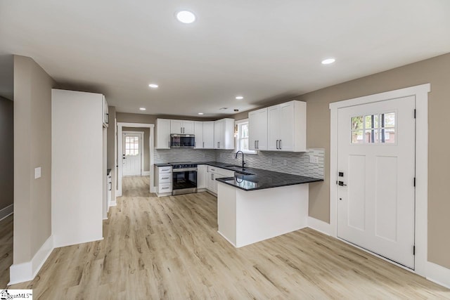 kitchen featuring kitchen peninsula, appliances with stainless steel finishes, backsplash, white cabinets, and light hardwood / wood-style floors